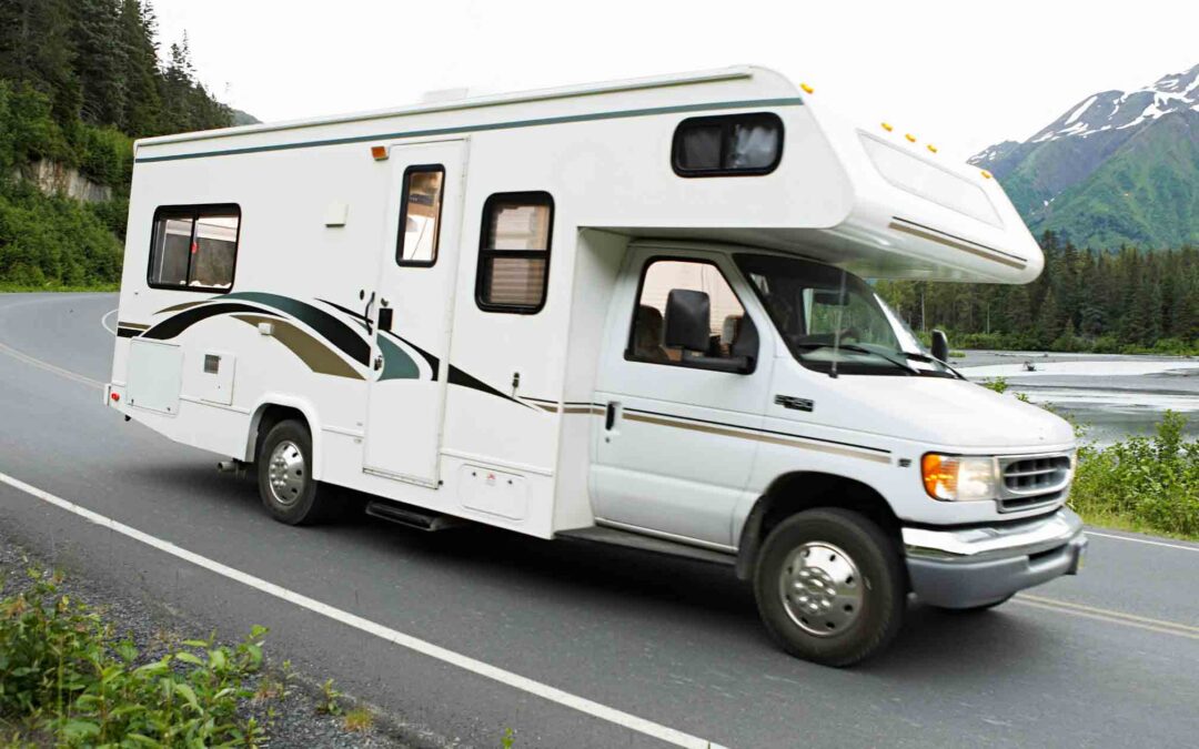 A white RV travels along a scenic road surrounded by greenery and trees.